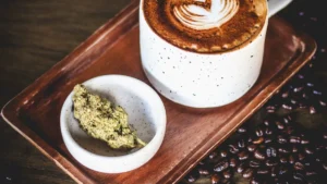 Cogollo de cannabis junto a una taza de bebida caliente sobre una bandeja de madera